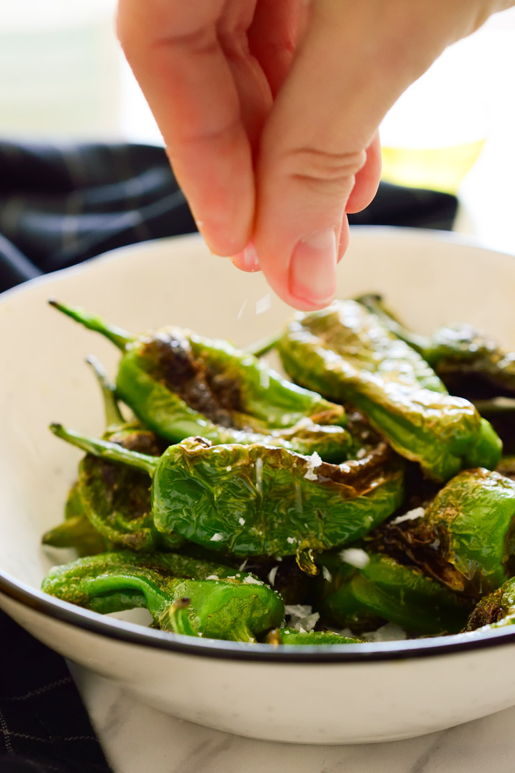 Sprinkling salt over padron peppers in a bowl.
