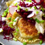 Estos pierogi polacos van camino de ser una de las empanadillas de patata más ricas que jamás hayas probado. Rellenos de patata, setas asadas, cebolla caramelizada y ajo, acompañados de crema agria vegana y chucrut; estos pierogi componen un plato delicioso y sustancioso para vegetarianos, veganos y omnívoros!