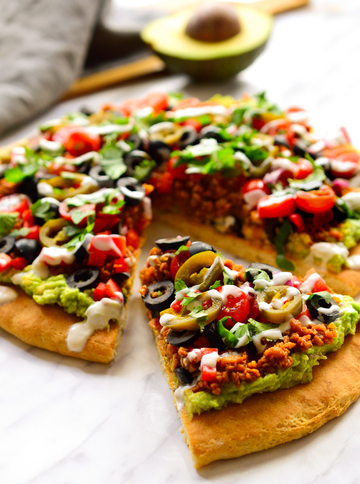 Esta pizza vegana representa el matrimonio entre dos de las mejores comidas en este mundo: pizza y nachos. ¿Cómo te quedas? Una masa de pizza cubierta de guacamole y decorada con carne vegana especiada, verduras, cilantro, jalapeños y un chorro de crema agria vegana. 