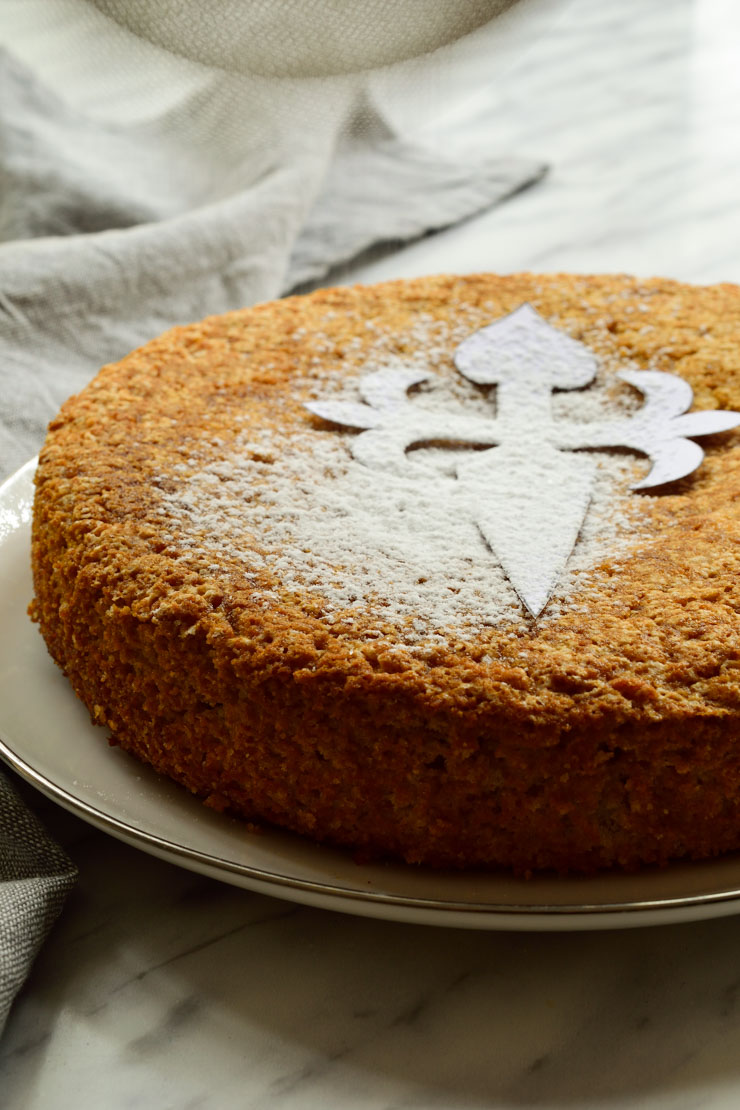 This Spanish almond cake is a vegan version of the traditional Tarta de Santiago from Galicia. This cake is easy to make with minimal ingredients and a clever egg substitute. Decorated with the Cross of Saint James and served with Spanish moscatel (or other sweet liqueur), this vegan Spanish almond cake makes a great dessert to a holiday or a regular weeknight dinner!