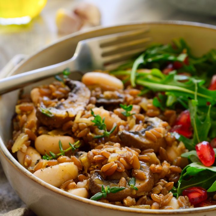 Mushroom farro with beans in a bowl with a rocket and pomegranate salad on the side.