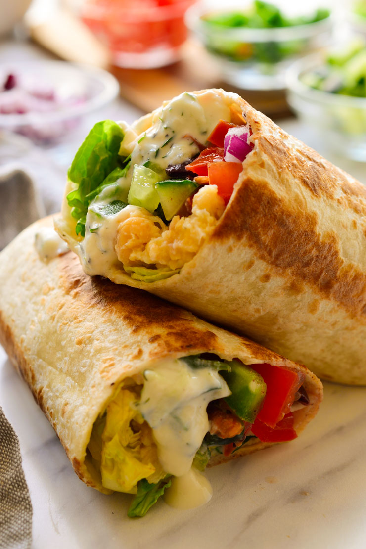 Burritos veganos mediterráneos cortados en dos en la encimera.