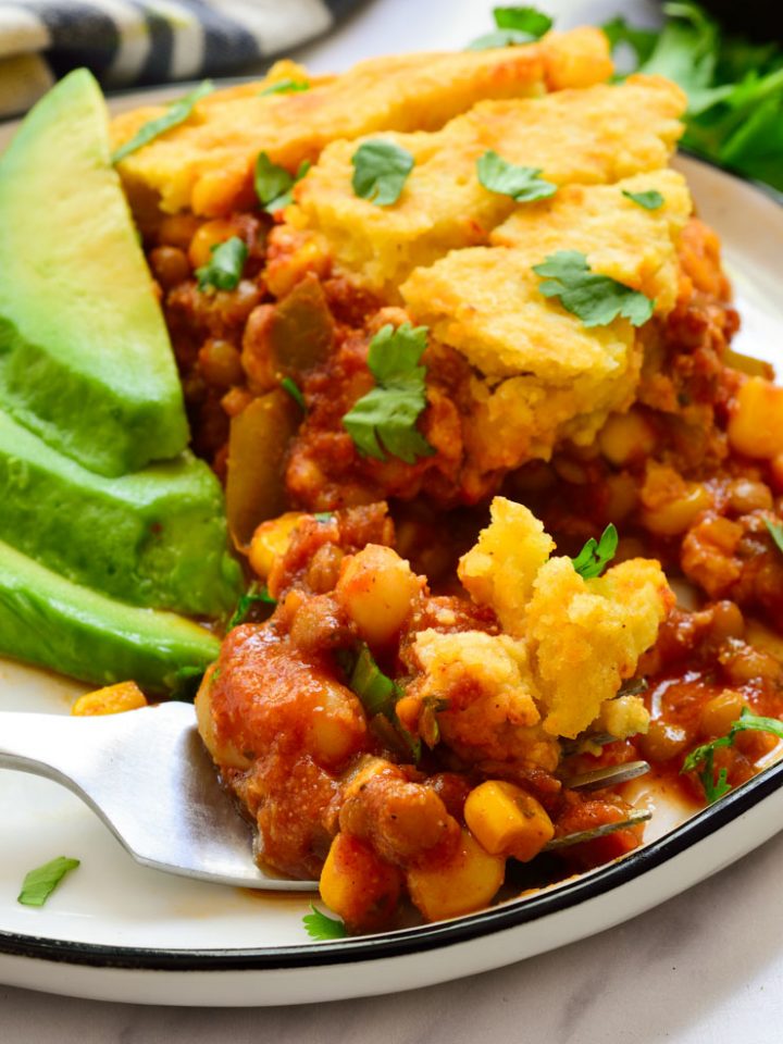 Vegan tamale pie on a plate served with avocado slices and fresh cilantro.