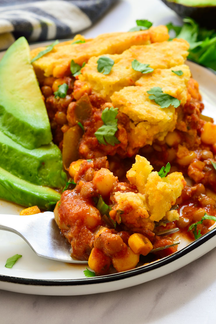 Vegan tamale pie on a plate served with avocado slices and fresh cilantro.