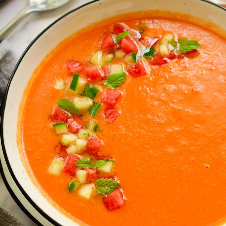 Watermelon gazpacho garnished with cucumber and diced watermelon in a white bowl