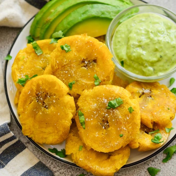 Patacones or tostones on a plate with avocado and green sauce.