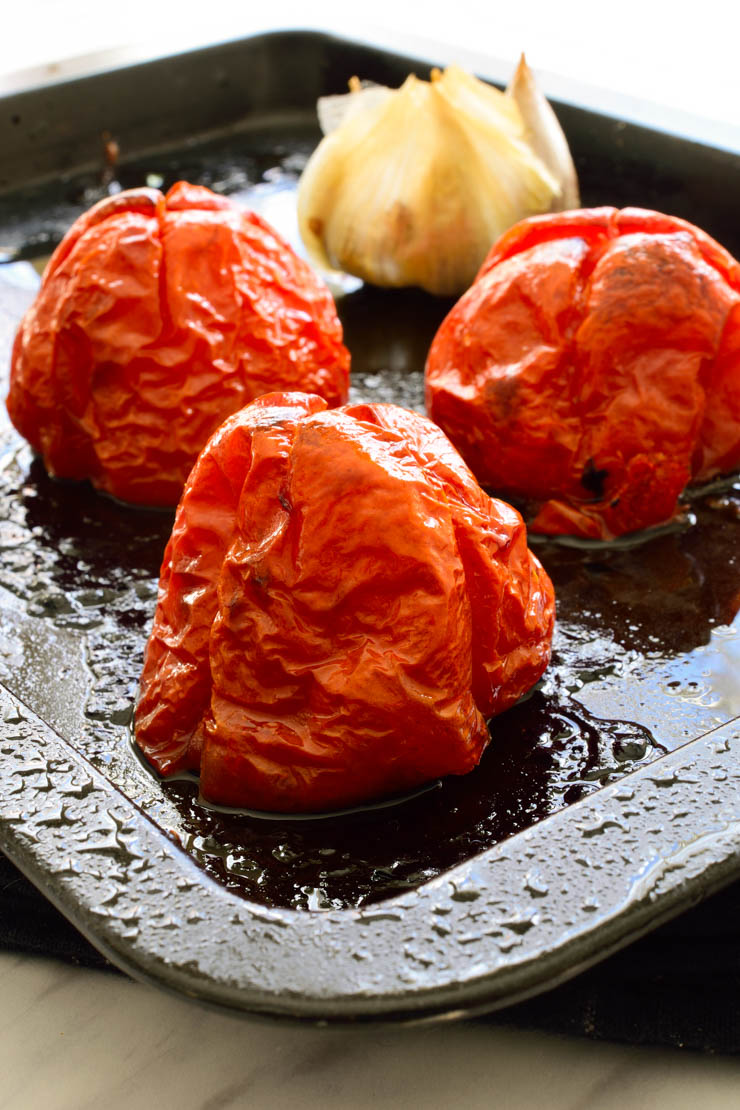 A pan with three roasted tomatoes and a head of garlic.