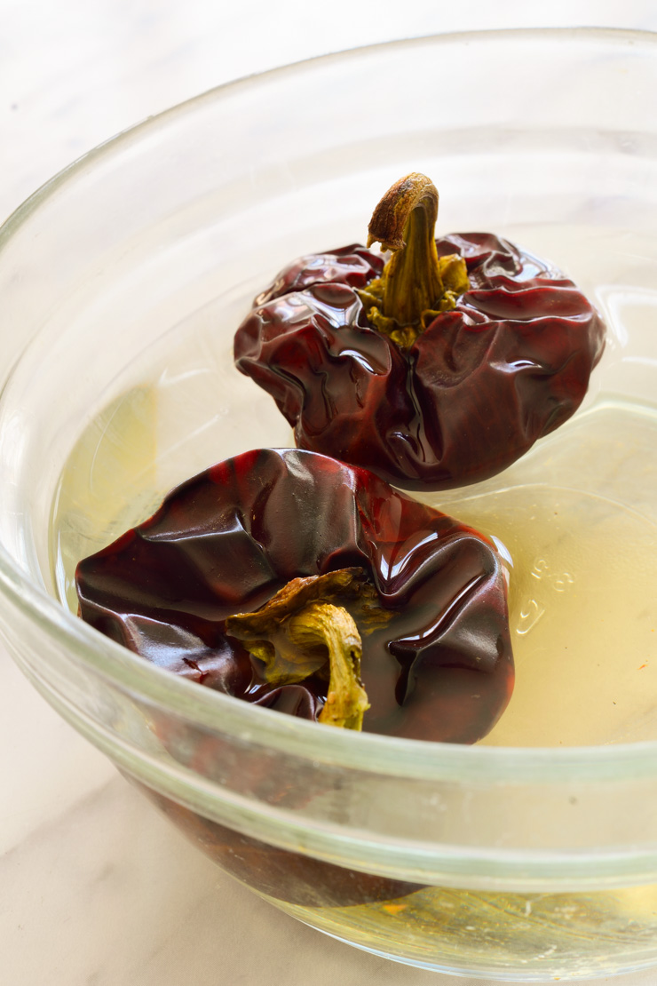 Two ñora peppers rehydrating in a bowl.