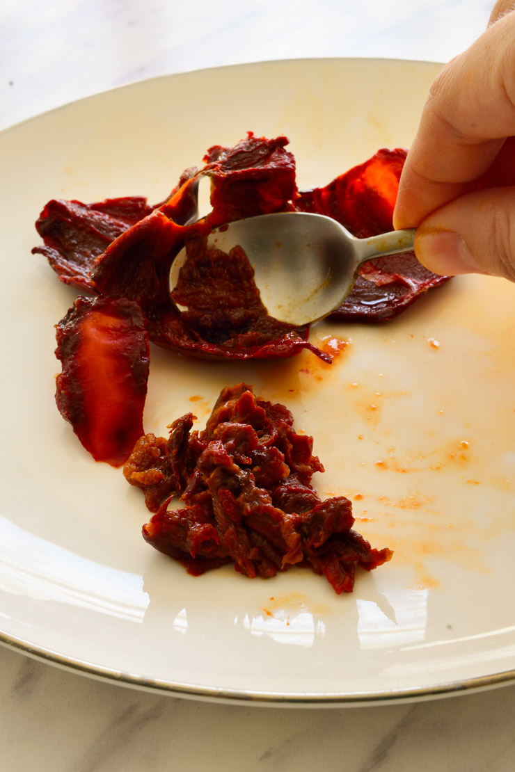 Scooping the pulp from ñora peppers with a spoon.