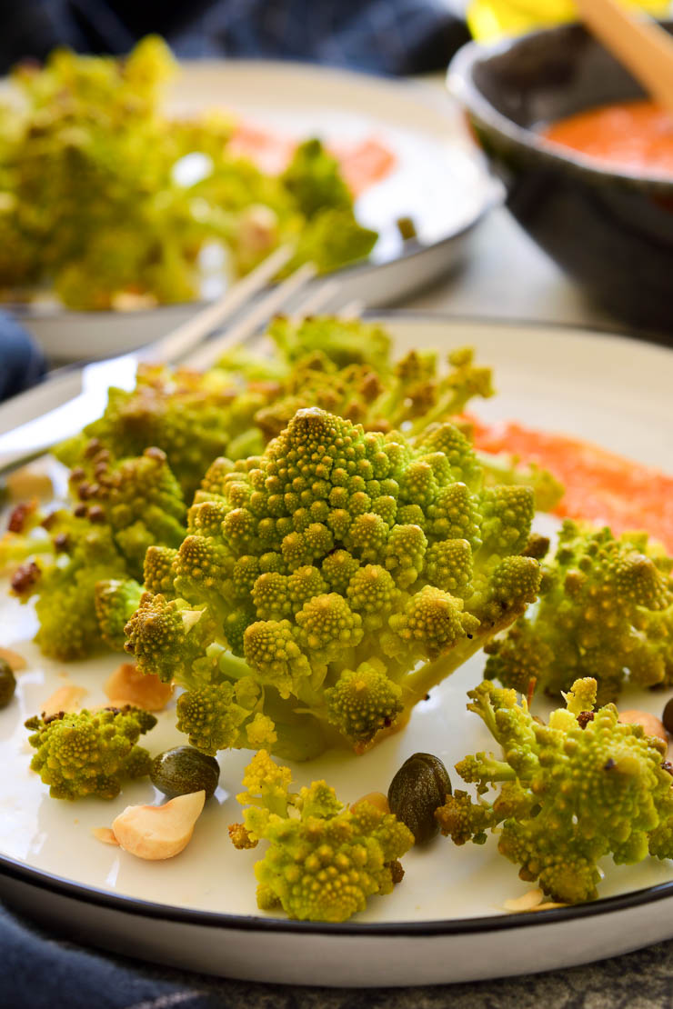 A plate of roasted romanesco florets with romesco sauce in the back.