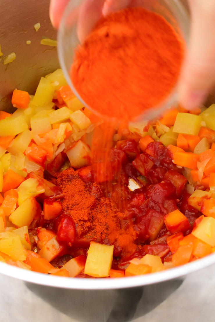 Sprinkling paprika into the pot of veggies.