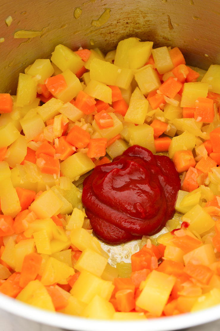 A pot of diced carrots and potatoes with a dollop of tomato paste in the middle.