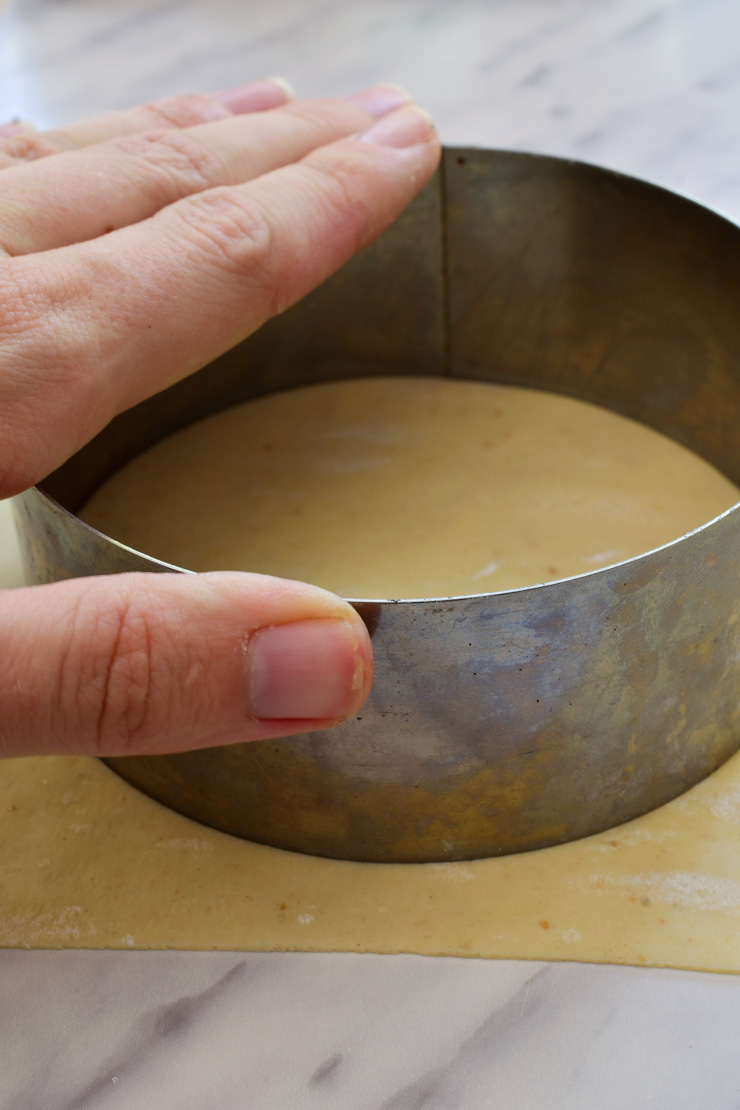 A hand using a metal ring to cut a circle out of the sheet of dough.