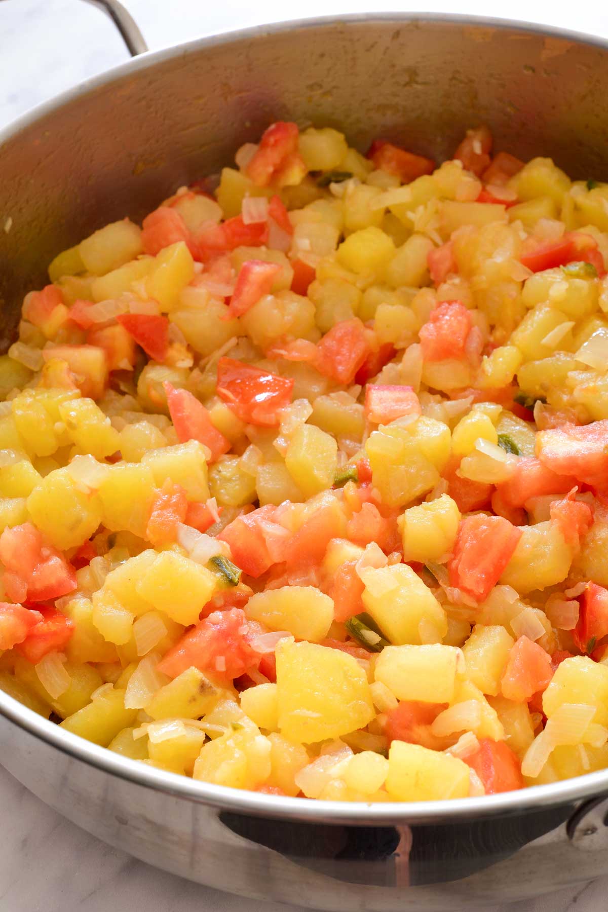 Fried diced potatoes, onions, garlic, jalapenos and tomatoes in a pan.